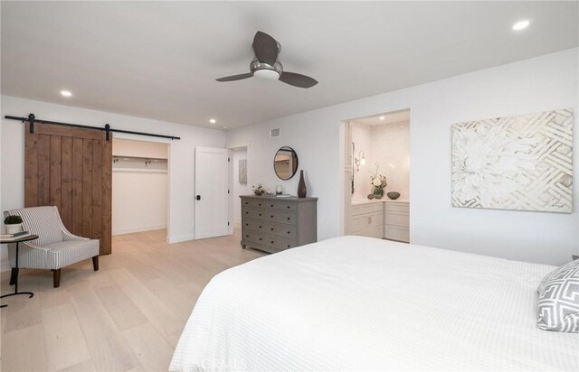 bedroom with ensuite bath, ceiling fan, a barn door, light hardwood / wood-style flooring, and a closet