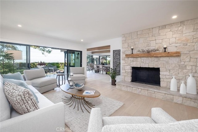 living room with light wood-type flooring, a stone fireplace, and plenty of natural light