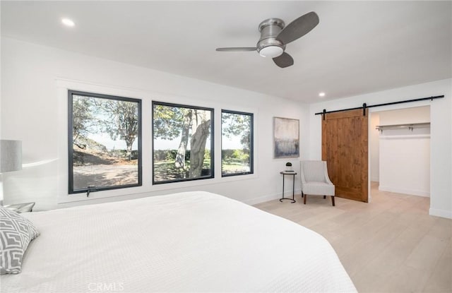 bedroom with a barn door, ceiling fan, and light wood-type flooring