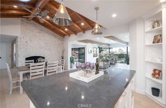 kitchen with white cabinets, lofted ceiling with beams, hanging light fixtures, dark stone countertops, and light wood-type flooring