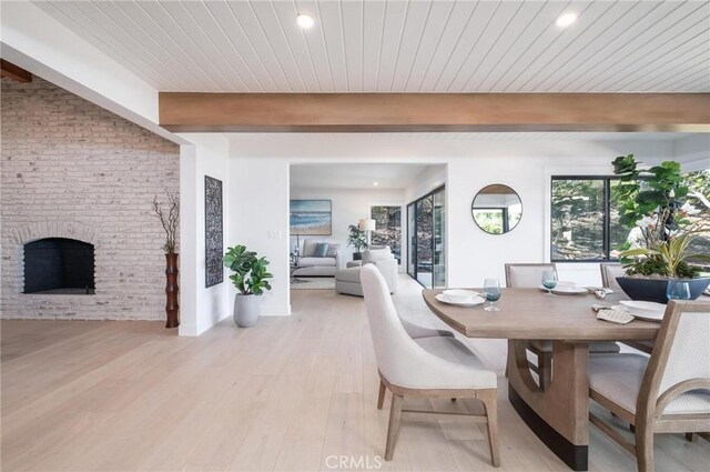 dining space with a brick fireplace, beam ceiling, wood ceiling, and light hardwood / wood-style flooring