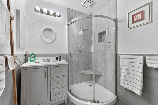 bathroom featuring a shower with door, vanity, and tile walls