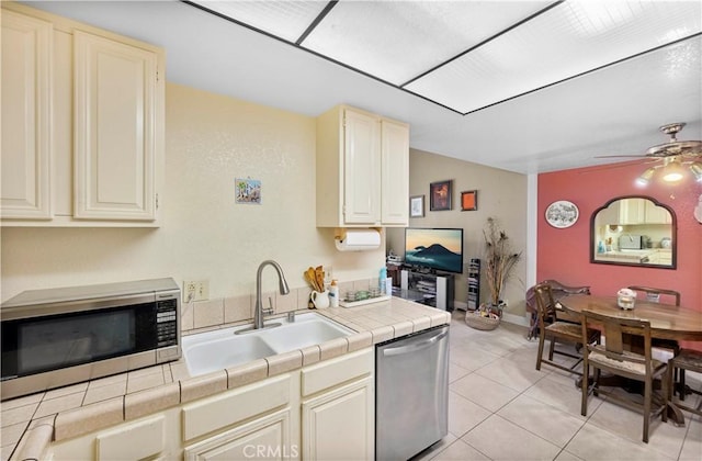 kitchen with light tile patterned floors, stainless steel appliances, tile counters, and sink