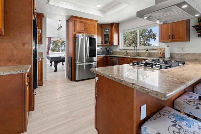 kitchen with stainless steel appliances, light stone counters, billiards, kitchen peninsula, and island range hood