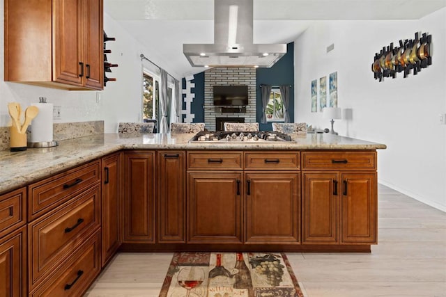 kitchen featuring wall chimney exhaust hood, stainless steel gas stovetop, light hardwood / wood-style floors, and light stone counters