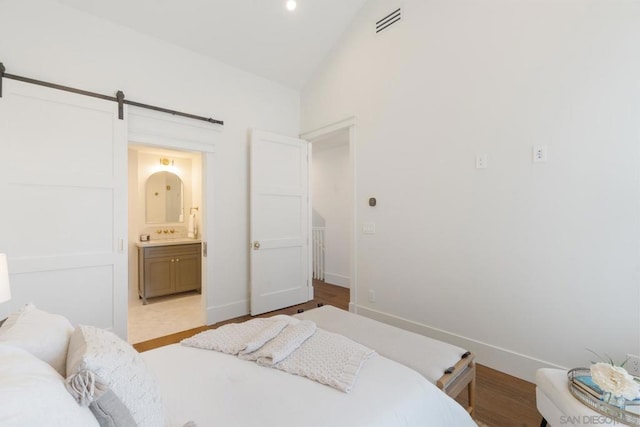 bedroom featuring a barn door, light hardwood / wood-style floors, connected bathroom, and vaulted ceiling