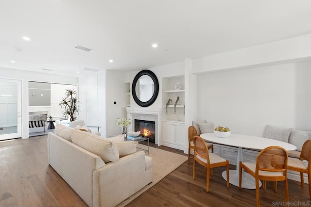 living room with built in shelves, a premium fireplace, and dark wood-type flooring