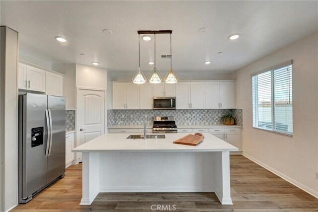 kitchen featuring a kitchen island with sink, sink, hanging light fixtures, white cabinetry, and stainless steel appliances