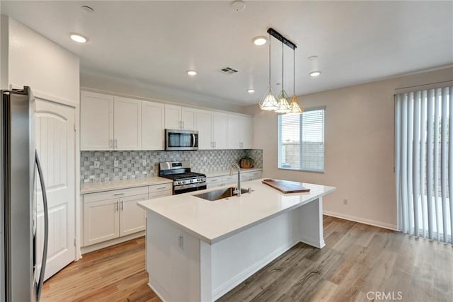 kitchen with white cabinets, sink, light hardwood / wood-style flooring, decorative light fixtures, and stainless steel appliances