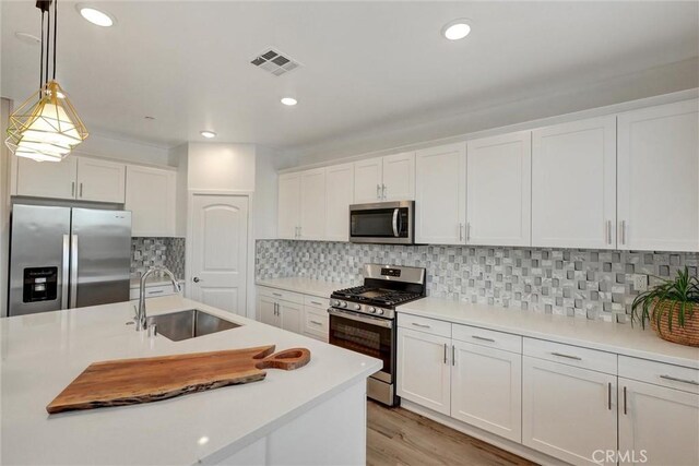 kitchen featuring white cabinets, sink, stainless steel appliances, and hanging light fixtures