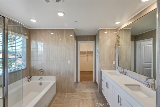 bathroom with a tub to relax in, tile patterned flooring, vanity, and tile walls