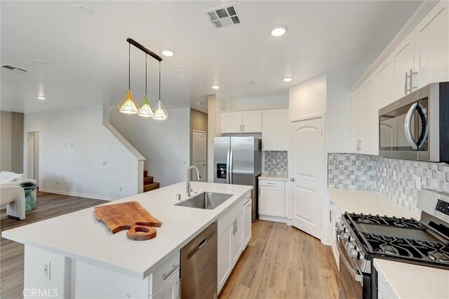 kitchen with a kitchen island with sink, sink, light wood-type flooring, appliances with stainless steel finishes, and white cabinetry