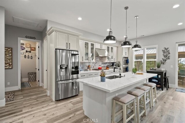 kitchen featuring pendant lighting, a center island with sink, sink, stainless steel appliances, and light stone counters