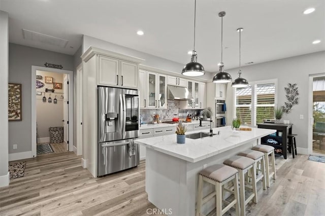 kitchen featuring stainless steel appliances, an island with sink, sink, hanging light fixtures, and light stone counters