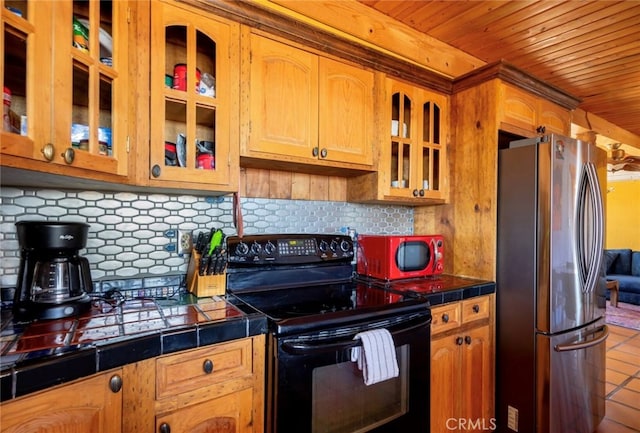 kitchen featuring black electric range oven, tasteful backsplash, wooden ceiling, stainless steel refrigerator, and tile counters