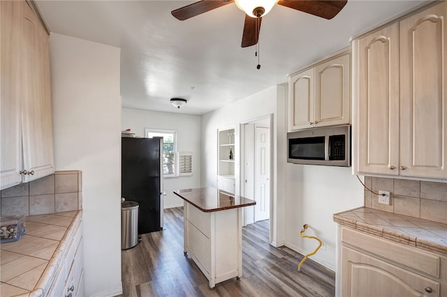 kitchen with black refrigerator, dark hardwood / wood-style flooring, backsplash, ceiling fan, and tile countertops