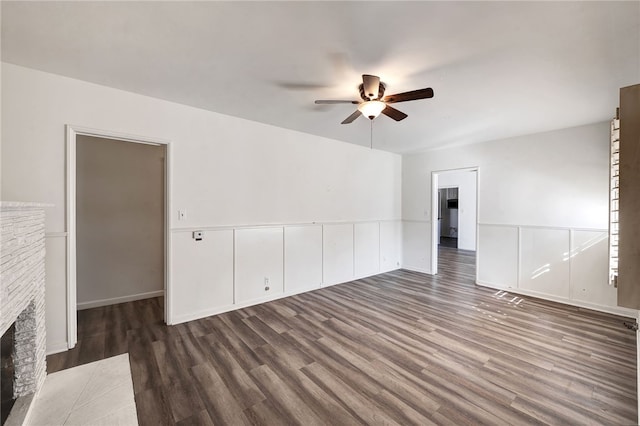 unfurnished living room with a stone fireplace, ceiling fan, and dark wood-type flooring