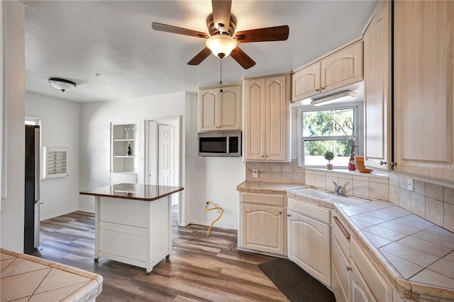 kitchen with tile countertops, backsplash, a kitchen island, wood-type flooring, and stainless steel appliances