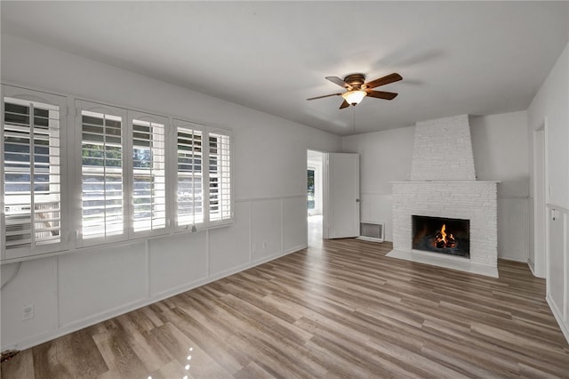 unfurnished living room featuring light wood-type flooring, a stone fireplace, and ceiling fan