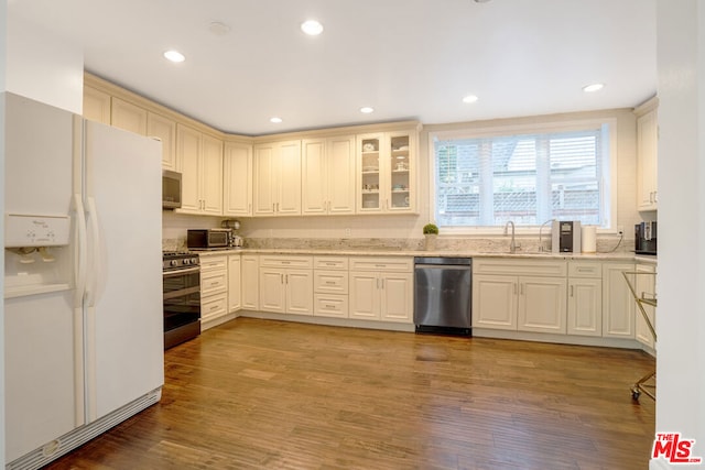 kitchen featuring appliances with stainless steel finishes, light hardwood / wood-style floors, light stone counters, and sink