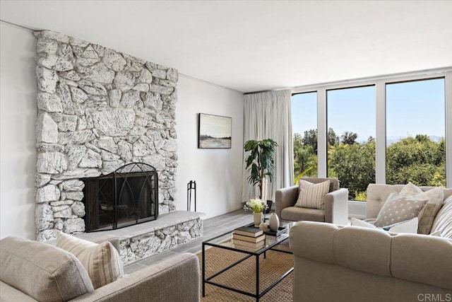 living room featuring a stone fireplace, wood-type flooring, and a healthy amount of sunlight