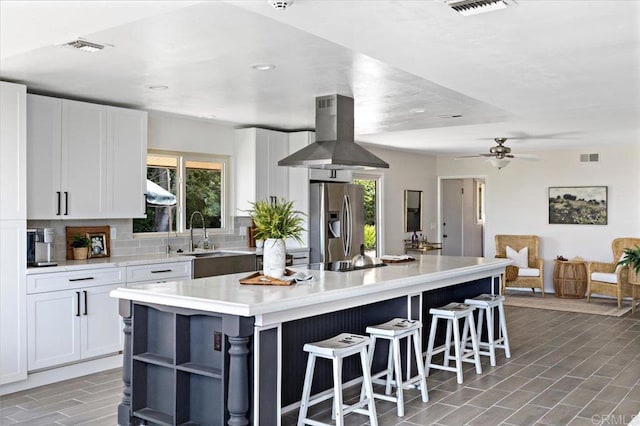 kitchen featuring island exhaust hood, stainless steel fridge, white cabinets, sink, and a center island