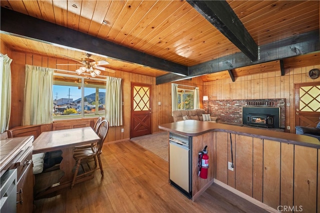 kitchen with beamed ceiling, a wood stove, wooden walls, and plenty of natural light