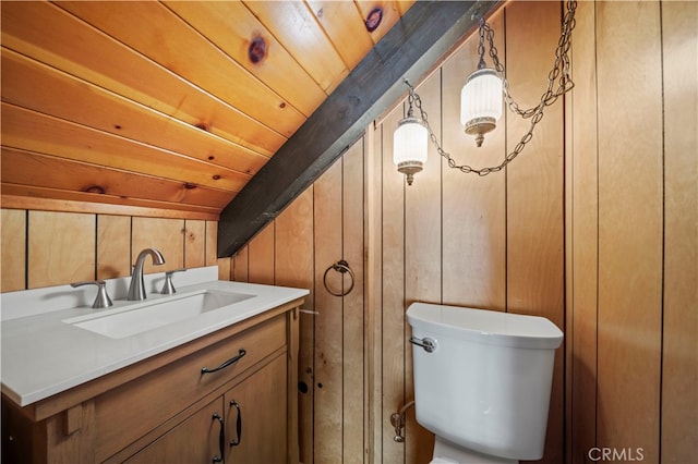 bathroom with vanity, toilet, wood walls, and wood ceiling