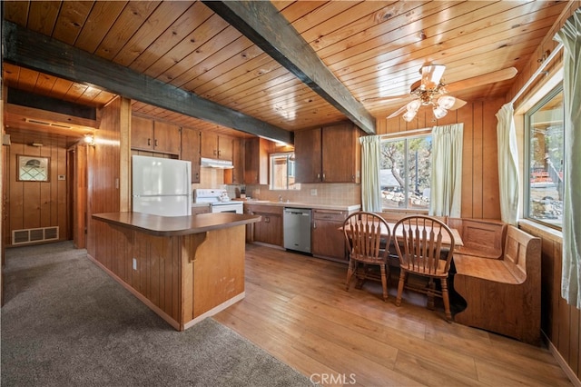 kitchen featuring beamed ceiling, wooden walls, light hardwood / wood-style flooring, kitchen peninsula, and white appliances