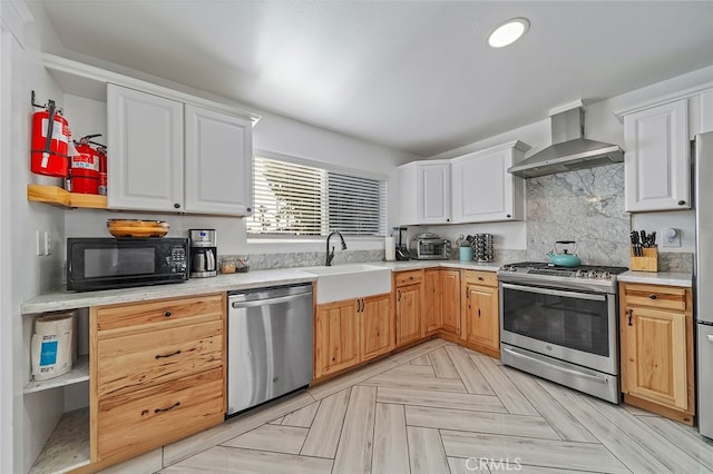 kitchen featuring appliances with stainless steel finishes, white cabinetry, sink, and wall chimney range hood