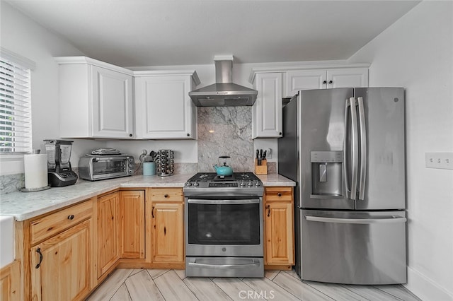 kitchen featuring wall chimney range hood, white cabinets, tasteful backsplash, appliances with stainless steel finishes, and light hardwood / wood-style floors