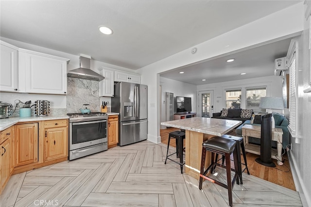 kitchen featuring wall chimney exhaust hood, a kitchen breakfast bar, stainless steel appliances, white cabinets, and tasteful backsplash