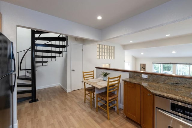 kitchen with light wood-type flooring, black fridge, dark stone counters, oven, and lofted ceiling