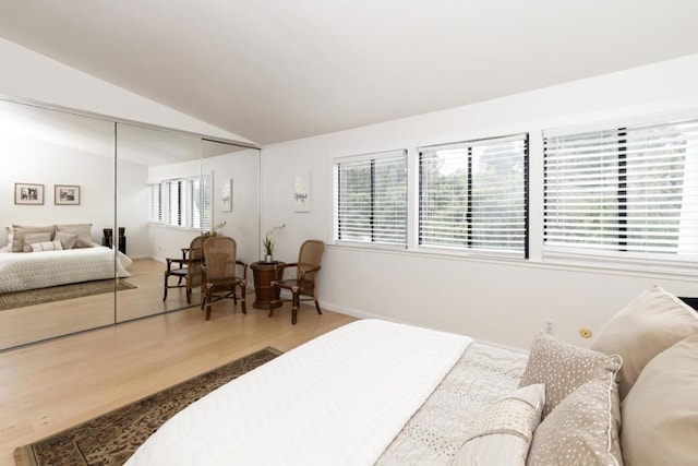 bedroom featuring hardwood / wood-style flooring, vaulted ceiling, a closet, and multiple windows