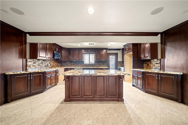 kitchen with tasteful backsplash, sink, dark brown cabinets, a center island, and light stone counters