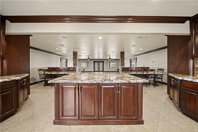 kitchen featuring light stone countertops, an island with sink, light tile patterned floors, and ceiling fan