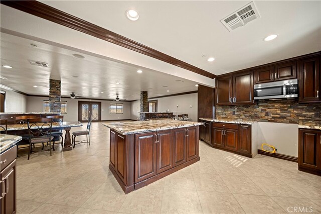 kitchen featuring light stone countertops, backsplash, dark brown cabinets, a center island, and ceiling fan