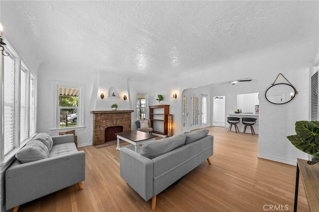 living room with a textured ceiling, light hardwood / wood-style flooring, and a stone fireplace