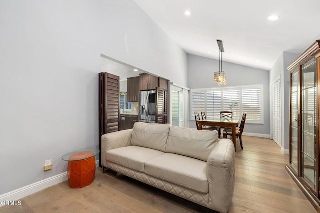 living room featuring a chandelier, light hardwood / wood-style floors, high vaulted ceiling, and a wealth of natural light