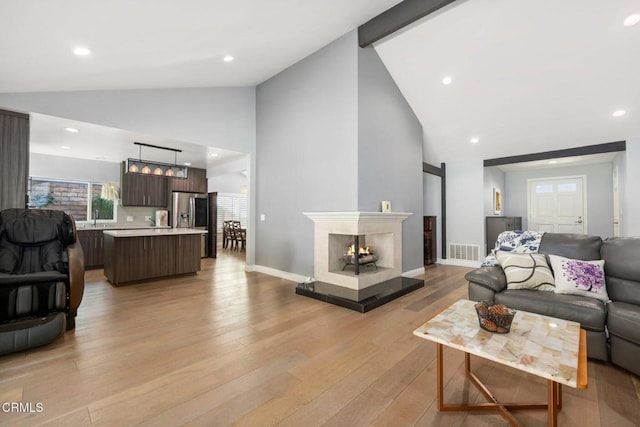 living room with sink, beamed ceiling, high vaulted ceiling, and light wood-type flooring