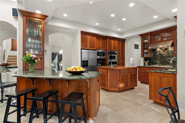 kitchen featuring extractor fan, a kitchen bar, appliances with stainless steel finishes, decorative backsplash, and a raised ceiling