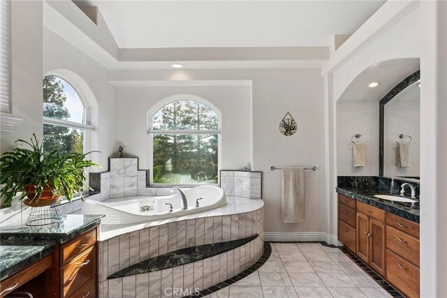 bathroom with tile patterned flooring, a relaxing tiled tub, and vanity