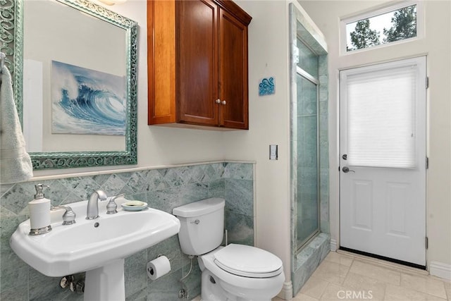 bathroom with tile walls, toilet, a shower with door, and tile patterned flooring