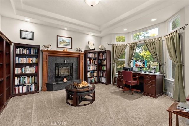 carpeted office with a tray ceiling and a fireplace