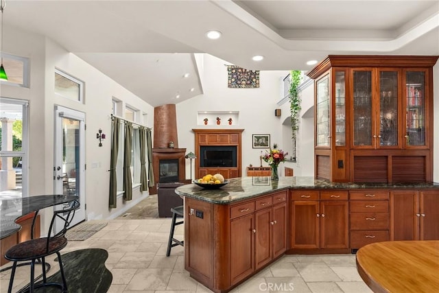 kitchen with a breakfast bar area, a large fireplace, dark stone countertops, and a raised ceiling