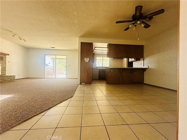 kitchen with a brick fireplace, ceiling fan, light tile patterned floors, a textured ceiling, and dark brown cabinets