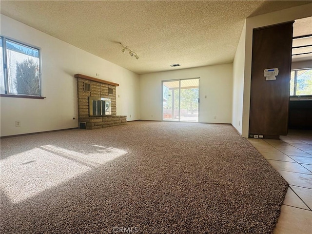 unfurnished living room with a wealth of natural light, light tile patterned flooring, a textured ceiling, and a brick fireplace