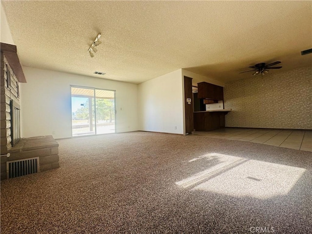 unfurnished living room featuring carpet flooring, ceiling fan, a fireplace, and a textured ceiling