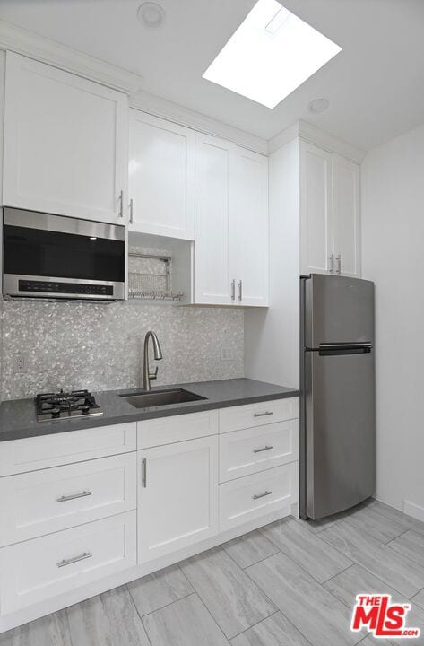 kitchen featuring sink, a skylight, tasteful backsplash, white cabinetry, and stainless steel appliances