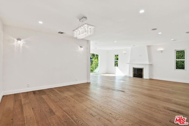 unfurnished living room featuring a notable chandelier, a large fireplace, and light hardwood / wood-style flooring